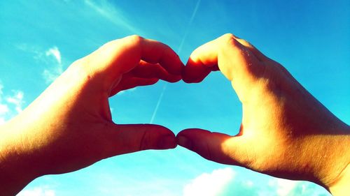 Cropped hands making heart shape against blue sky
