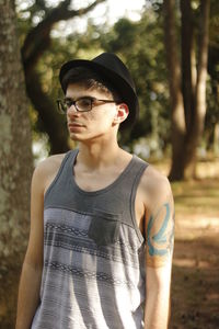 Thoughtful man wearing hat and eyeglasses at forest