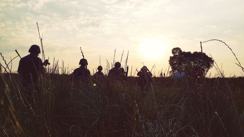 Rear view of silhouette hunters walking on field during sunset