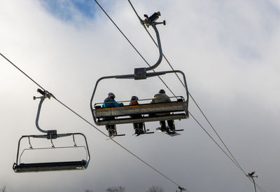 Rear view of three people riding on a ski lift to snowboard and ski down mount snow n vermont.