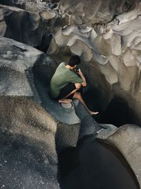 High angle view of man using mobile phone while sitting on rock