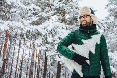 Young man standing by tree during winter