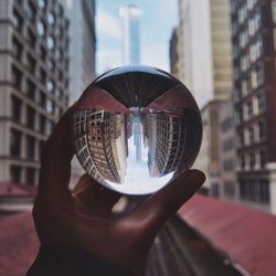 Cropped image of person holding crystal ball with reflection of buildings