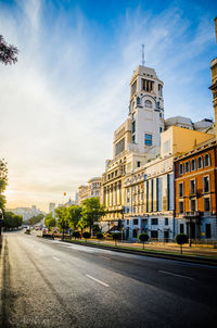 Empty road in city against cloudy sky