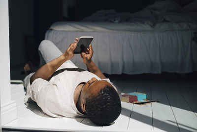 Mid adult man using mobile phone while lying on floor in sunlight at home