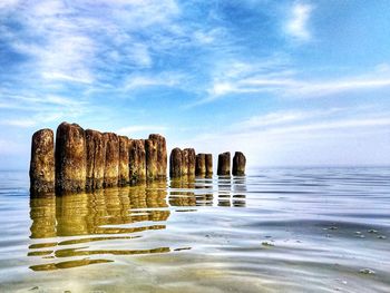 Wooden posts in sea against sky