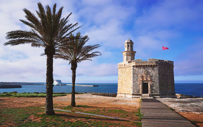 Palm trees by lighthouse at beach against sky