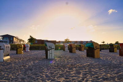 Hooded beach chairs against sky during sunset