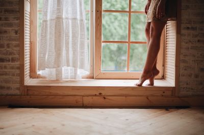 Low section of woman standing by window at home