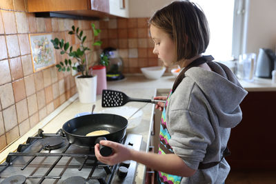 A girl cooks pancakes in the kitchen