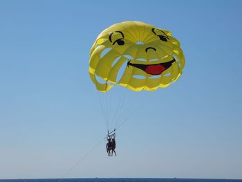 Low angle view of smiley face parachute flying against clear sky