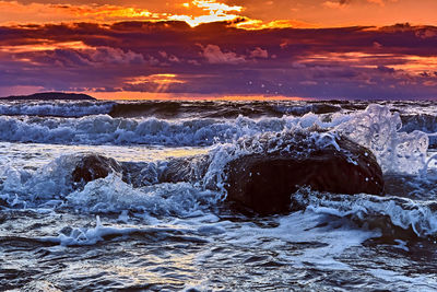 Water splashing in sea against sky during sunset