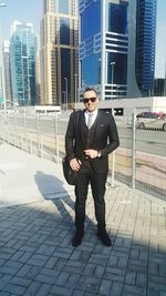 Full length portrait of young man standing against buildings in city