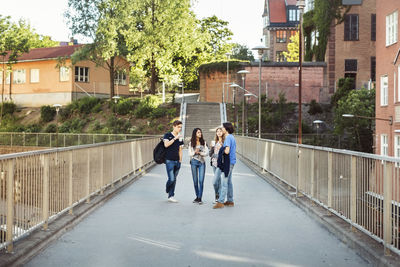 Full length of teenagers talking while standing on bridge in city