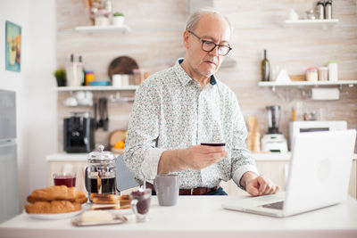 Senior man holding credit cart while using laptop at home