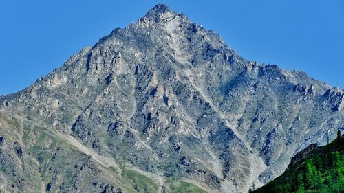 Low angle view of rocky mountains against clear blue sky