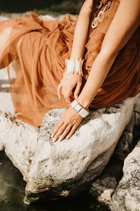 Low section of woman sitting on rock on the river with sensual hands and bijoux 