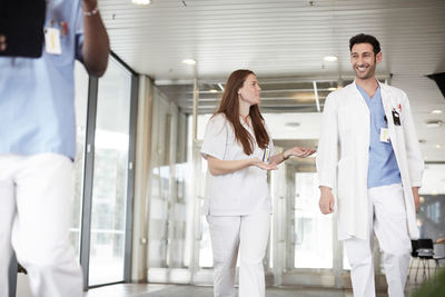 Smiling young healthcare workers discussing while walking in lobby at hospital