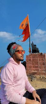 Young man wearing sunglasses sitting against flag