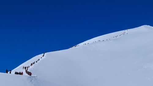 Low angle view of people on snowcapped mountain against clear blue sky