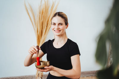 Portrait of young woman with arms raised standing against wall