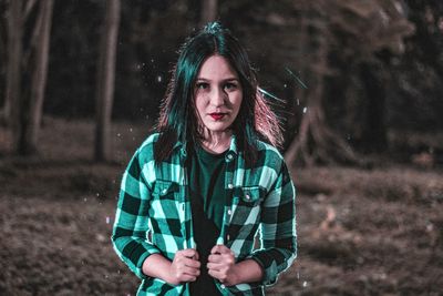 Portrait of young woman standing on field in forest