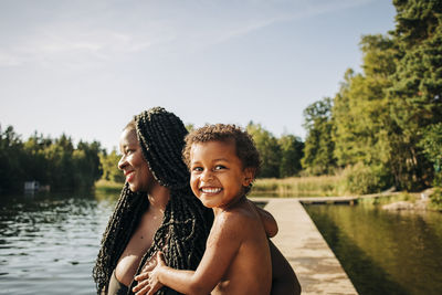 Smiling woman carrying excited son at lake during vacation