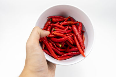 Close-up of hand holding red chili peppers over white background