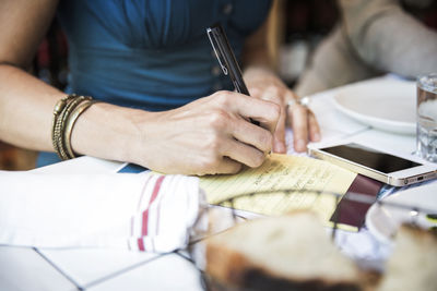 Midsection of woman writing on notepad while sitting in bar