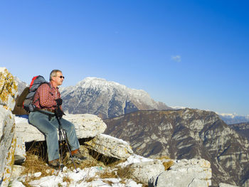 Man sitting on rock while hiking on mountain against sky