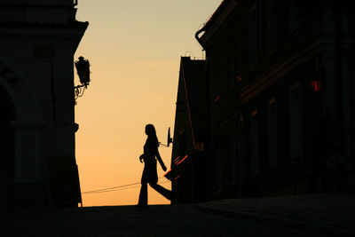 Silhouette man standing by building against sky during sunset