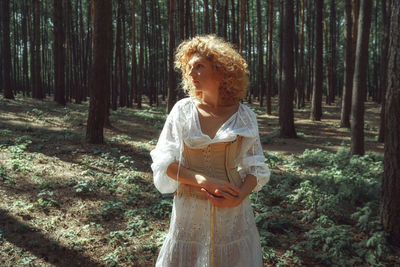 Woman standing by tree trunk in forest