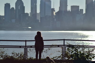 Rear view of woman standing by railing against sea and buildings