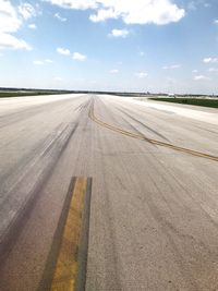 Road passing through airport runway against sky