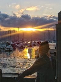 Rear view of man looking at harbor against sky during sunset