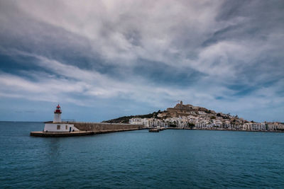 Lighthouse amidst sea and buildings against sky