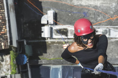 A woman wearing a hero costume with protective helmet walking down a tall rappel building. 