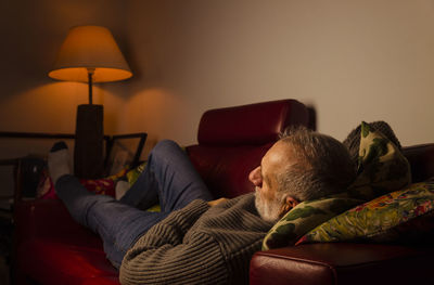 Adult man lying on sofa in living room at night