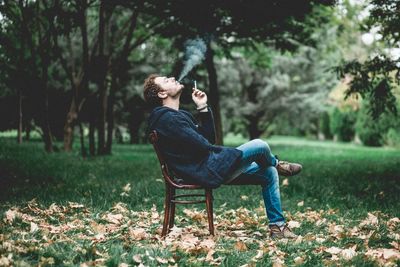 Side view of man sitting on bench in park