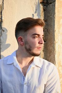 Young man looking away while standing against wall