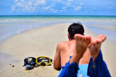 Rear view of shirtless man relaxing on beach