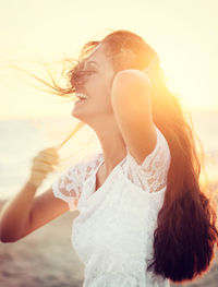 Close-up of smiling young woman standing against sea during sunset