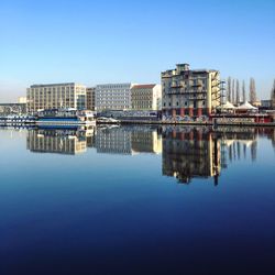 Reflection of buildings in lake against clear blue sky