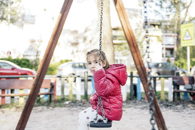 Portrait of girl sitting on swing at park