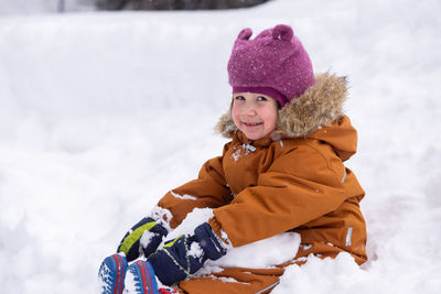 Portrait of smiling boy sitting on snow covered field
