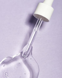 Top view of glass pipette with transparent hyaluronic acid serum for skin care placed in light room