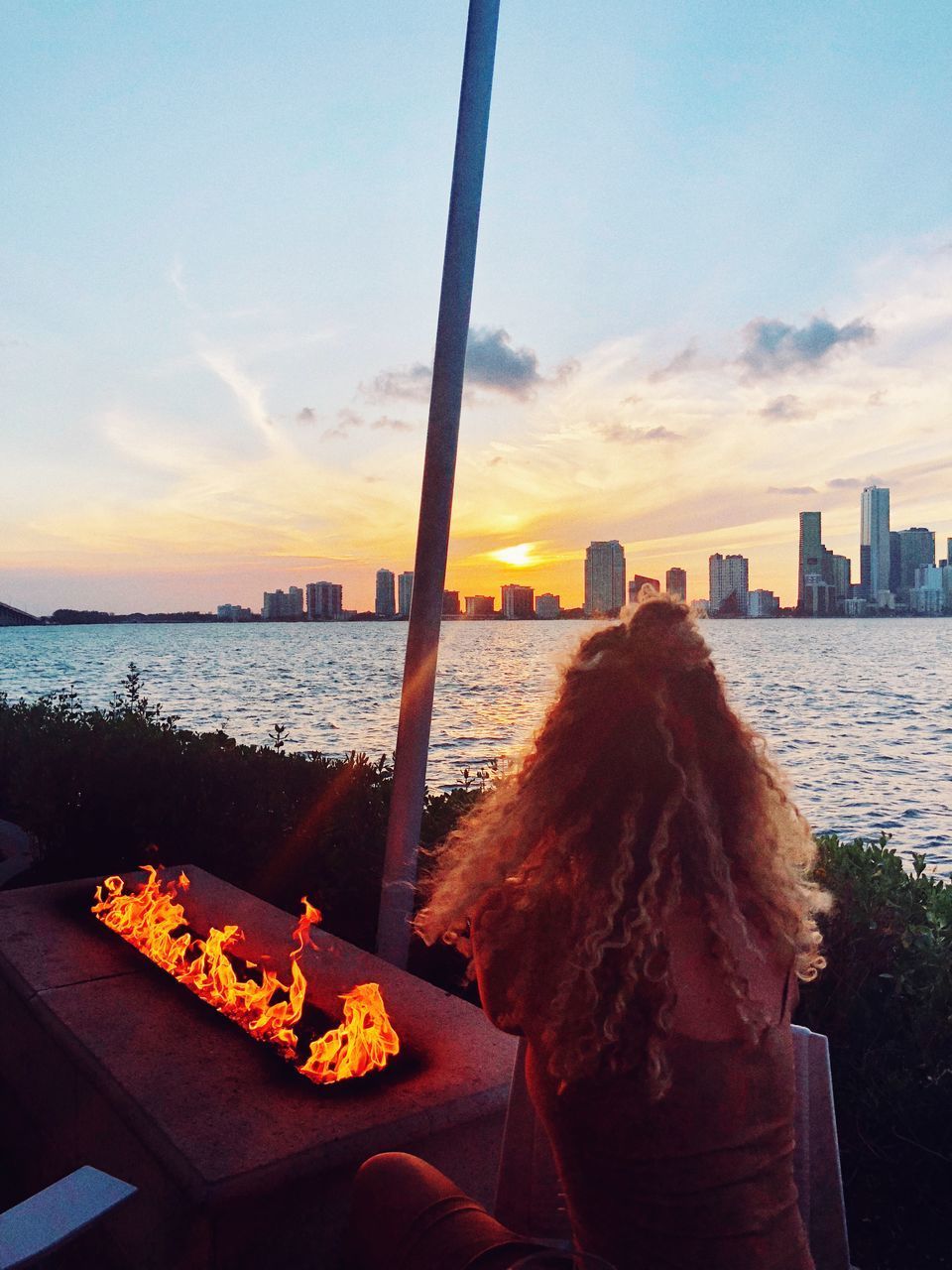 REAR VIEW OF WOMAN LOOKING AT CITY AGAINST SKY DURING SUNSET