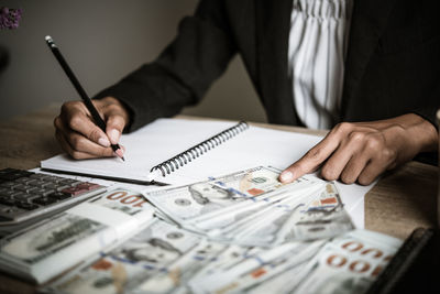 Midsection of businessman writing in book while counting money on table