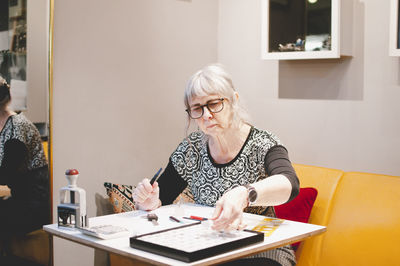 Senior female jeweler making jewelry at desk in workshop