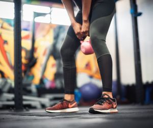 Low section of young woman lifting kettlebell at gym